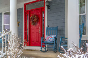 Residential home in Springfield, IL with blue siding, a newly painted red door, and blue rocking chairs on the patio in the winter