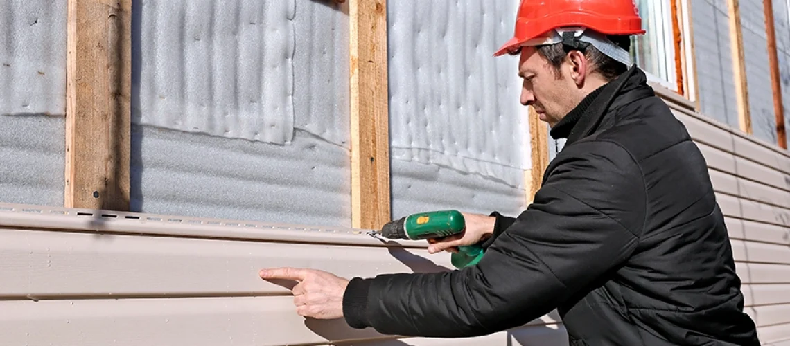 A worker professionally installs vinyl siding on the façade of this residential home in Springfield, IL.